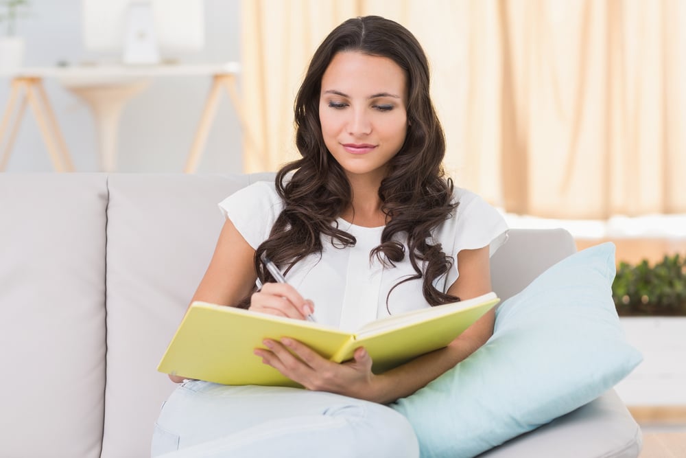 Pretty brunette writing on couch at home in the living room