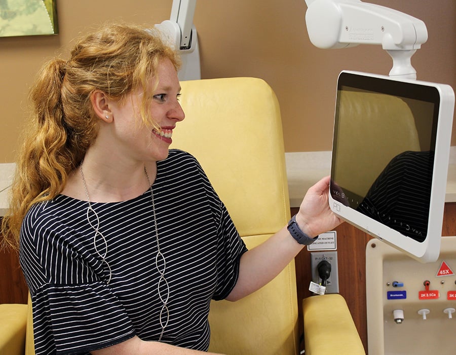 A dialysis patient using a PDi medTV16 device attached to a mounting arm on their dialysis chair.