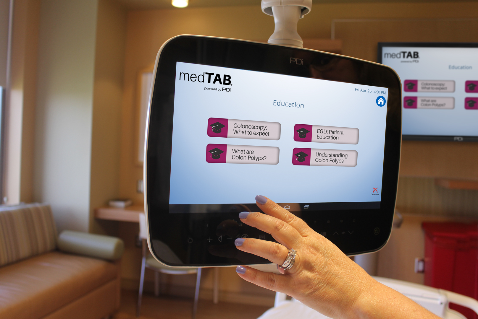 A medTAB14 by PDi Communication Systems, Inc, mounted by a patient bedside with a patients hand operating the screen with a display of patient education with a PDi large screen television in the background displaying the same image